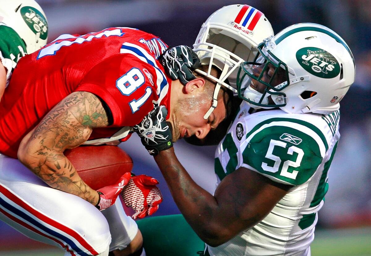 A football player, his white helmet perched on his head, grabs another football player's chest.