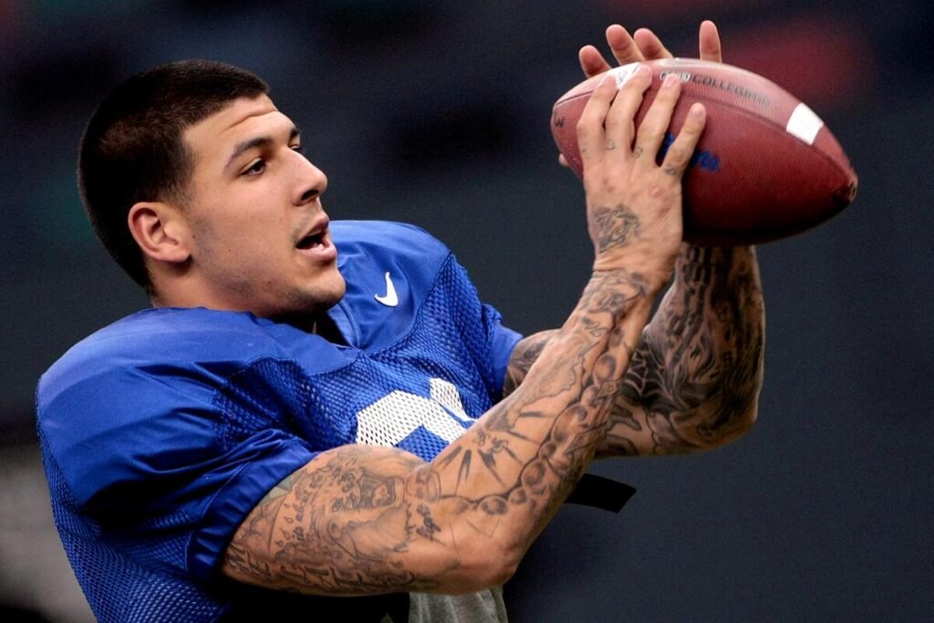 A soccer player with many tattooed arms in a blue jersey and patches, holding a soccer ball in his hands near his face.